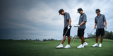 Three golfers in striped shirts and dark shorts on a golf course with a cloudy sky.